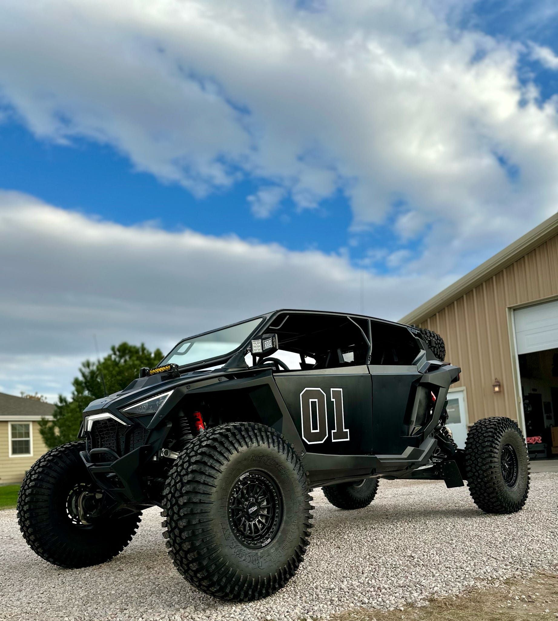 Black off-road vehicle with large tires on a gravel driveway under a blue sky.